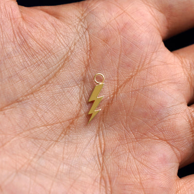 A solid gold Lightning Bolt Charm for earring resting in a model's palm