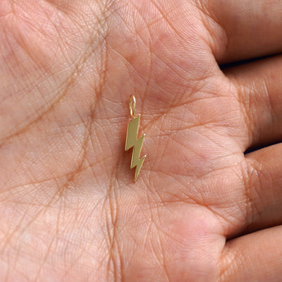 A solid gold Lightning Bolt Charm for chain resting in a model's palm