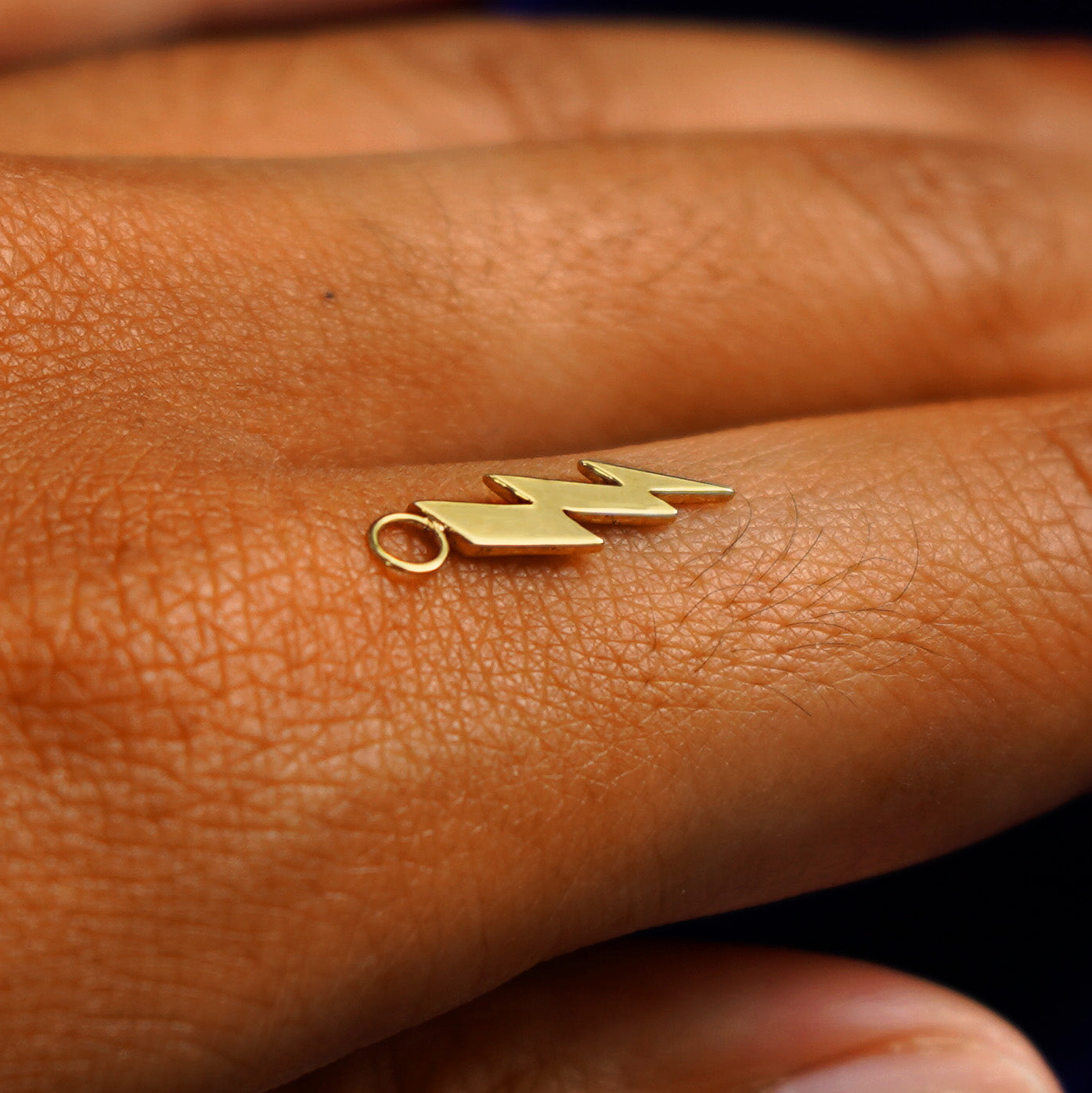 A 14k yellow gold Lightning Bolt Charm for earring balancing on the back of a model's finger