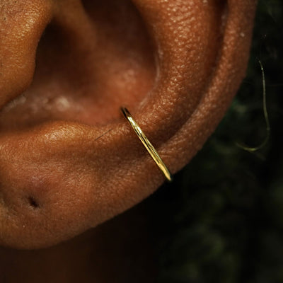 Close up view of a model's ear wearing a solid 14k yellow gold Line Cuff