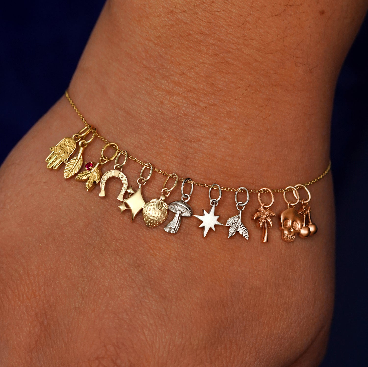 A model's wrist wearing a cable bracelet with various good luck and nature themed charms in different 14k gold colors