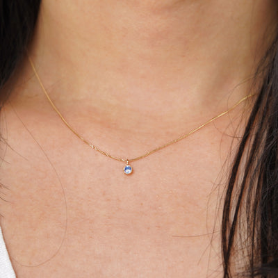 A model's neck wearing a solid 14k yellow gold Aquamarine necklace