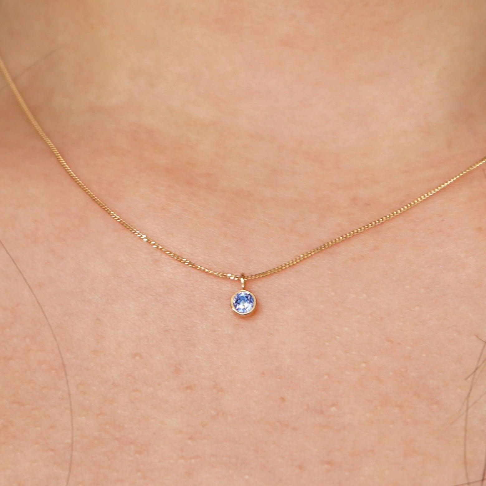Close up view of a model's neck wearing a solid 14k yellow gold Aquamarine necklace