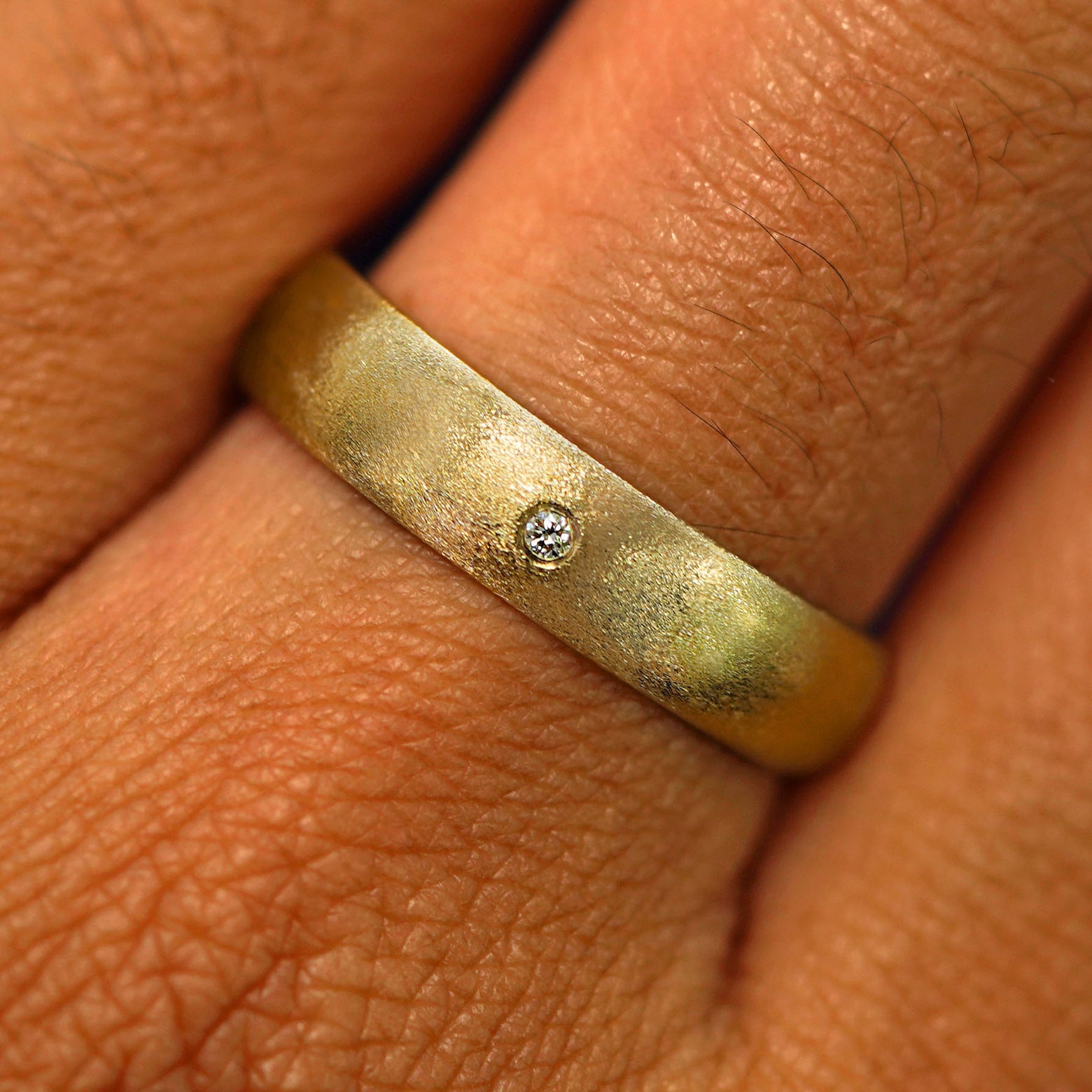 Close up view of a model's hand wearing a solid yellow gold Curvy Matte Band with one diamond