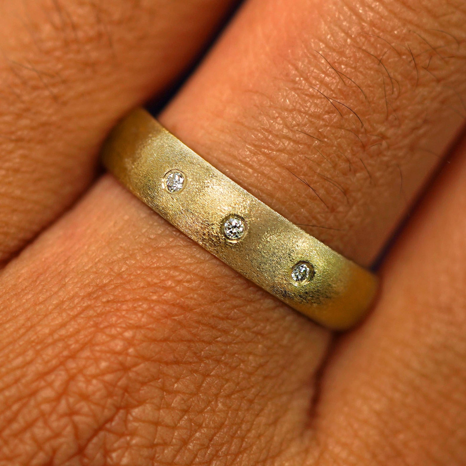 Close up view of a model's hand wearing a solid yellow gold Curvy Matte Band with three diamonds