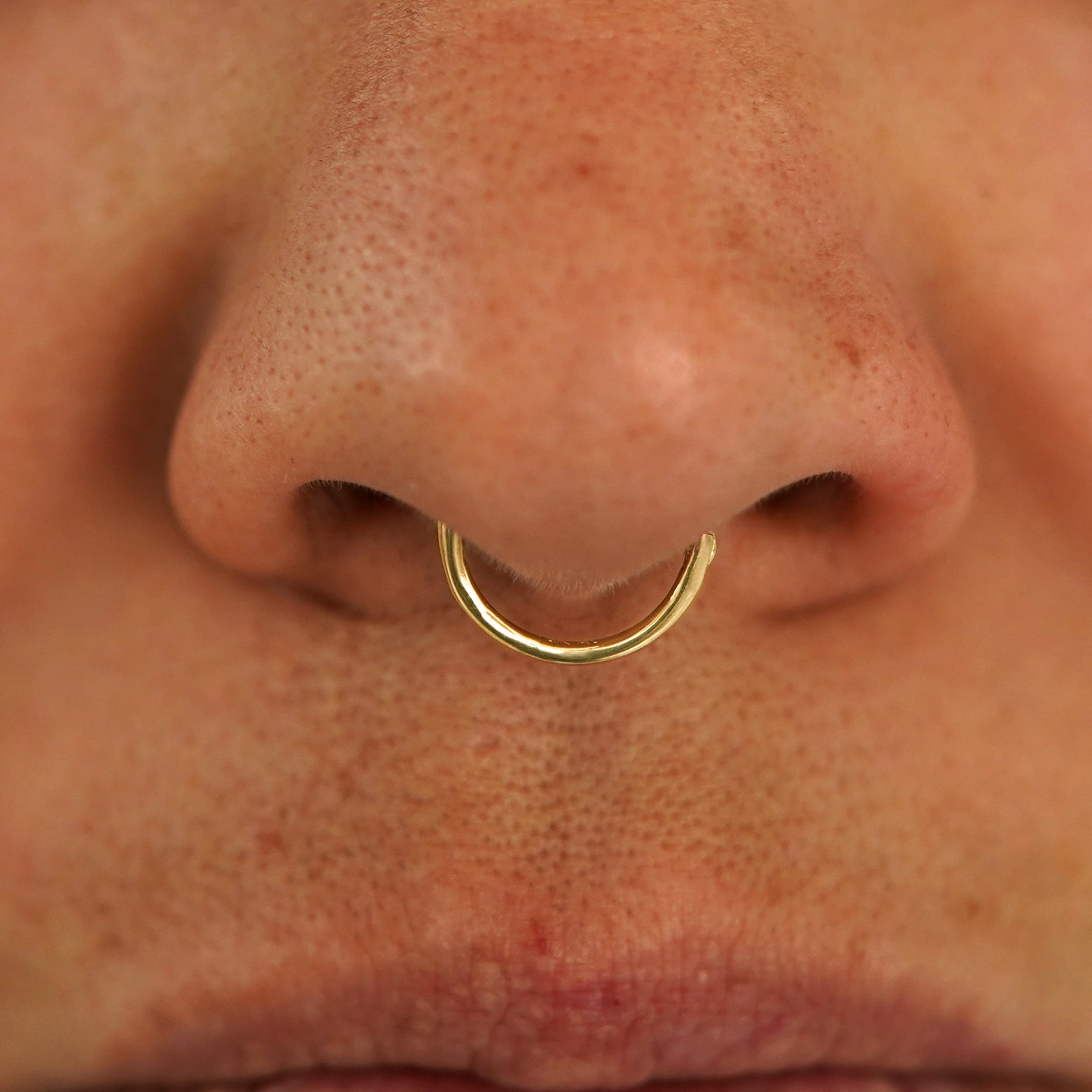 Close up view of a model's nose wearing a 14k yellow gold Medium Seamless Huggie Hoop in a septum piercing