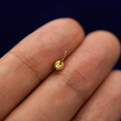 A yellow gold Medium Ball Earring laying facedown on a model's fingers to show the underside view