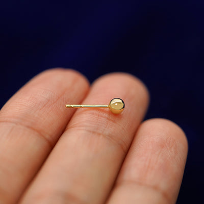 A 14k gold Medium Ball Earring sitting sideways on a model's fingertips to show detail