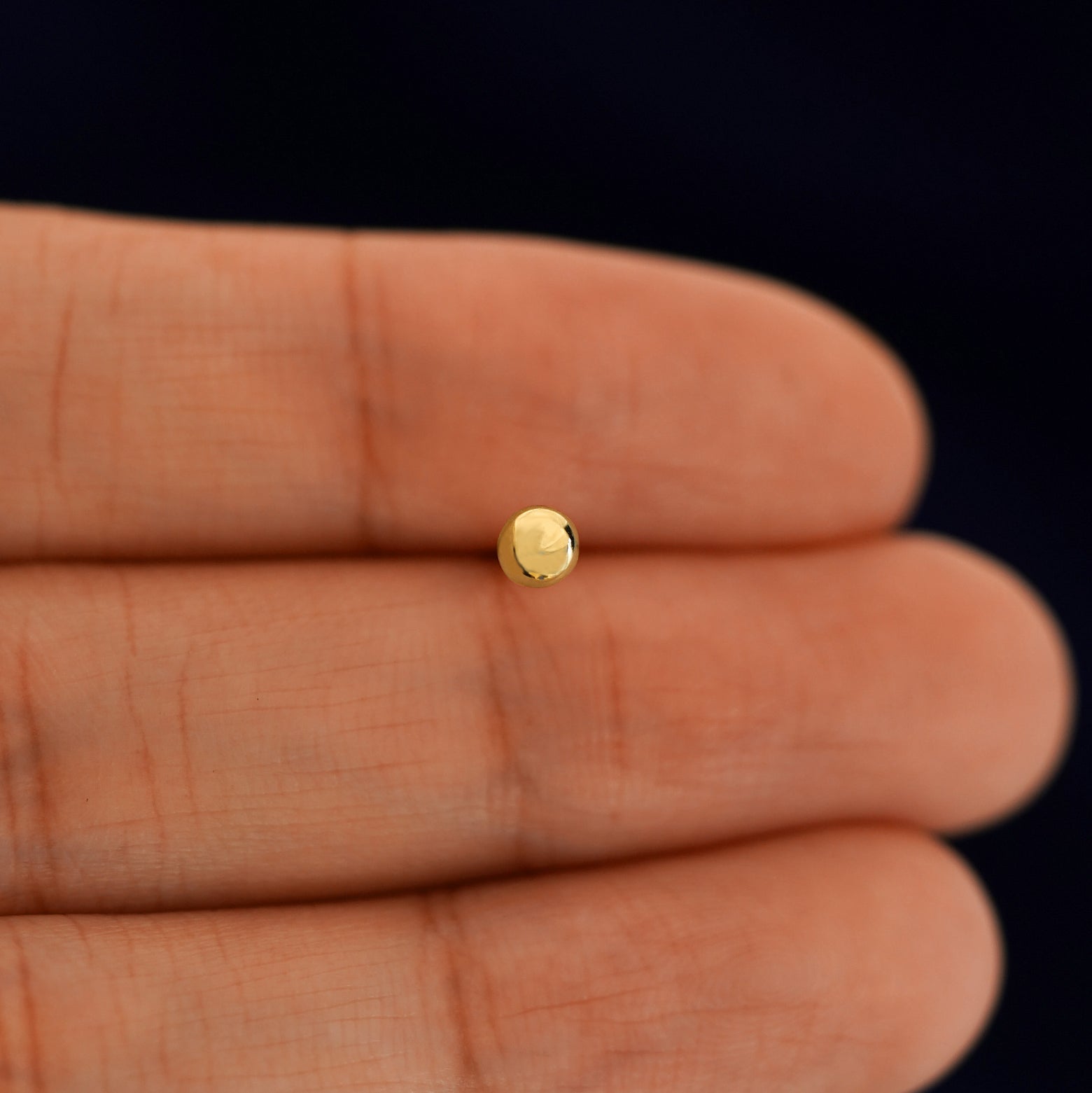 A solid 14k yellow gold Medium Ball Earring in between a model's fingers