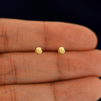 A pair of solid 14k yellow gold Medium Ball Earring in between a model's fingers