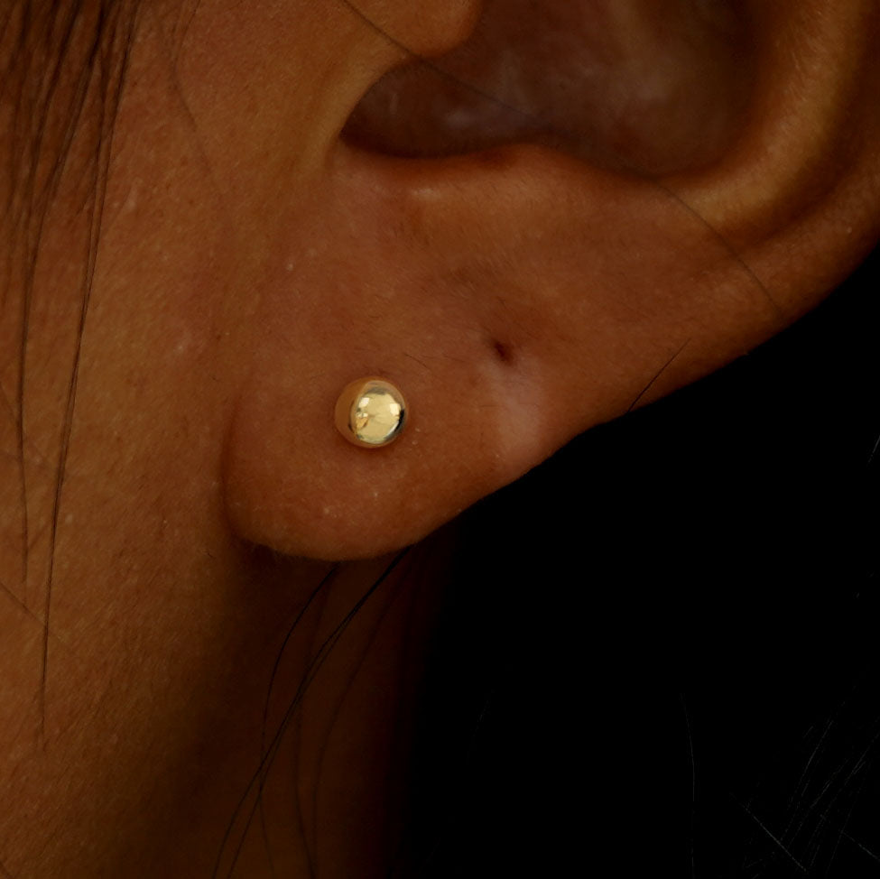 Close up view of a model's ear wearing a yellow gold Medium Ball Flatback Piercing