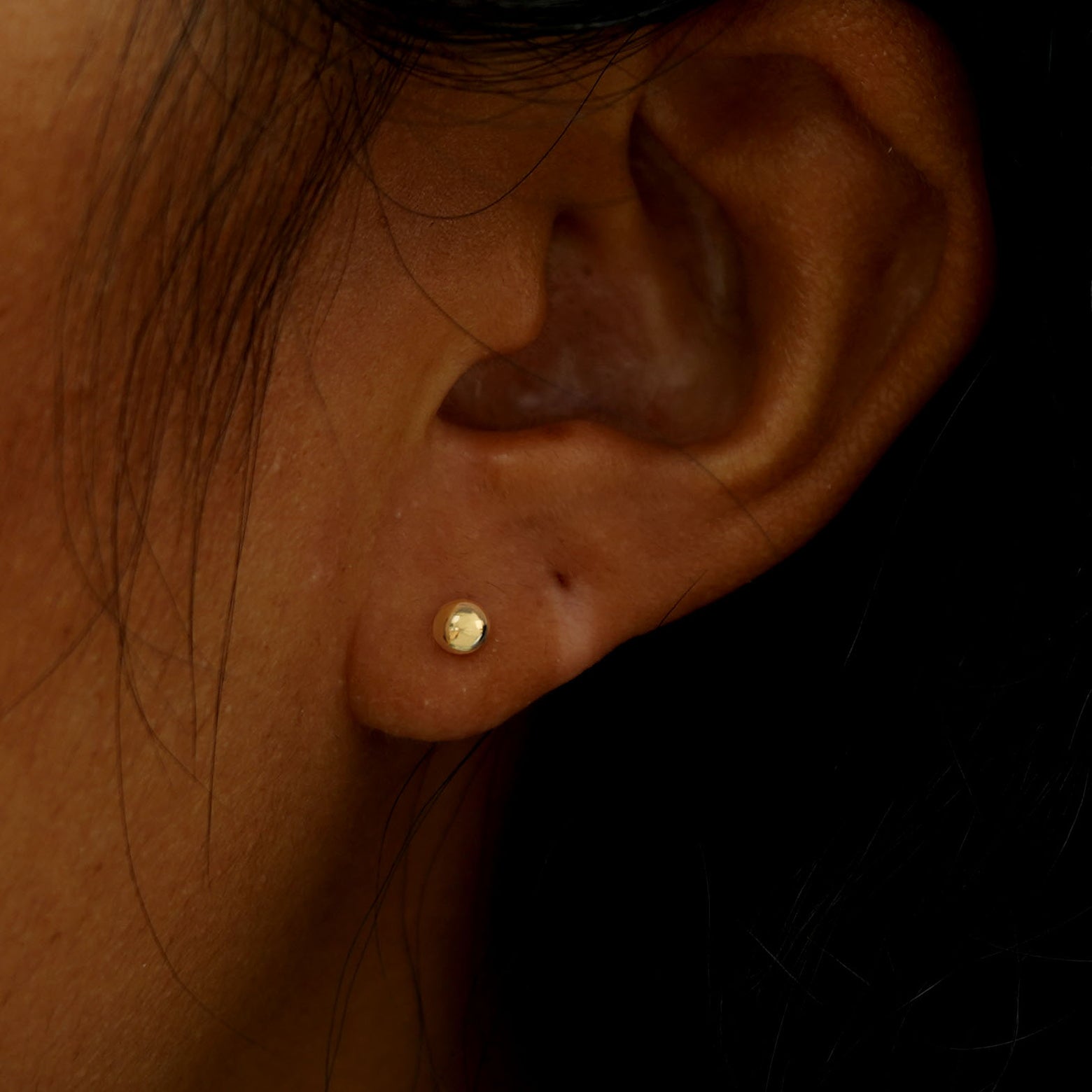 A model's ear wearing a solid yellow gold Medium Ball Flatback Piercing