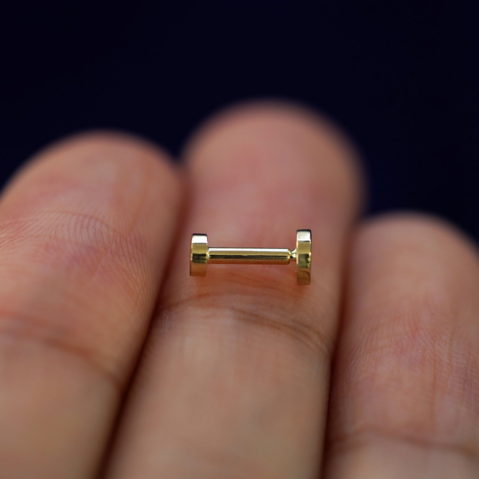 Side view of a yellow gold Medium Circle Flatback Piercing on a model's fingertips