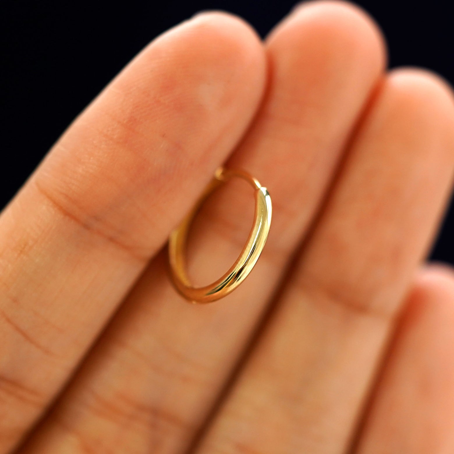 A 14k gold Medium Curvy Huggie Hoop Earring held in between a model's fingers to show the hoops thickness