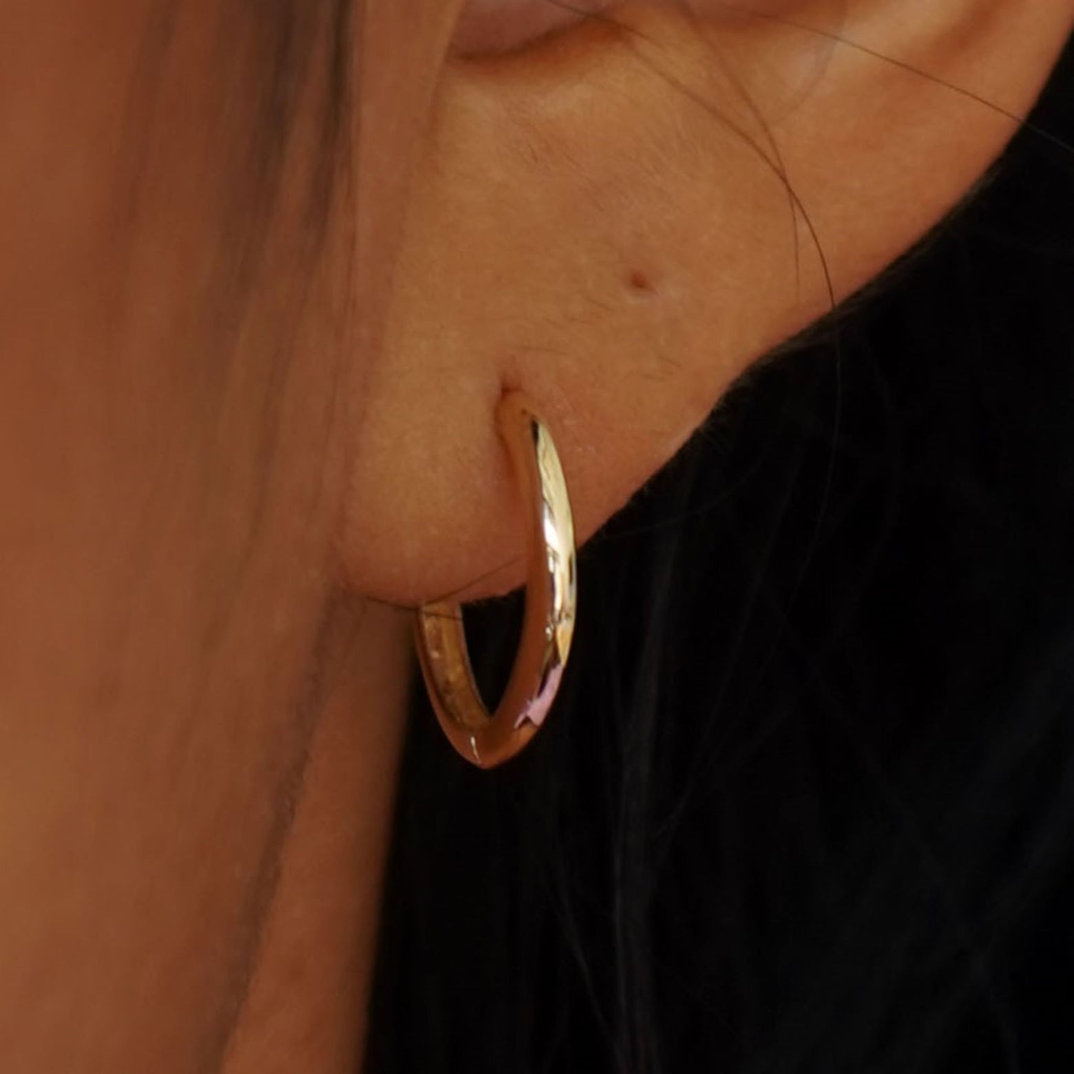 Close up view of a model's ear wearing a yellow gold Medium Curvy Huggie Hoop