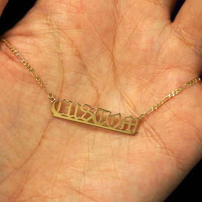 A 14k yellow gold custom nameplate necklace resting in a model's palm