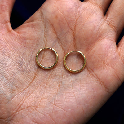 A pair of 14k gold Medium Curvy Huggie Hoop Earring sitting in a model's palm