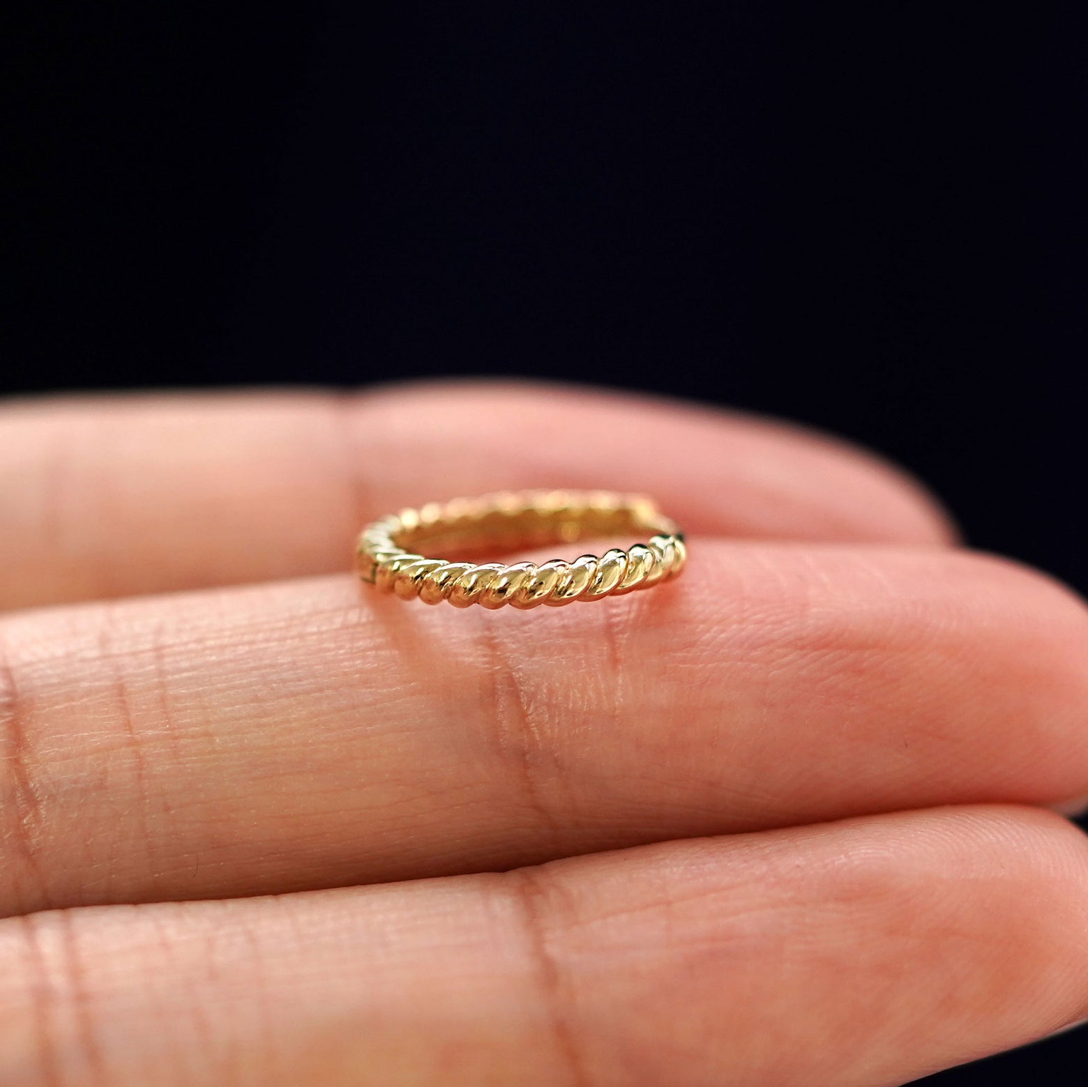 A yellow gold Medium Rope Huggie Hoop Earring laying sideways on a model's fingertips