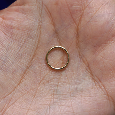 A model holding a closed yellow gold Medium Seamless Huggie Hoop in their palm