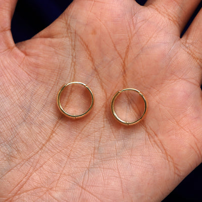 A pair of 14k gold Medium Thick Huggie Hoop Earring sitting in a model's palm