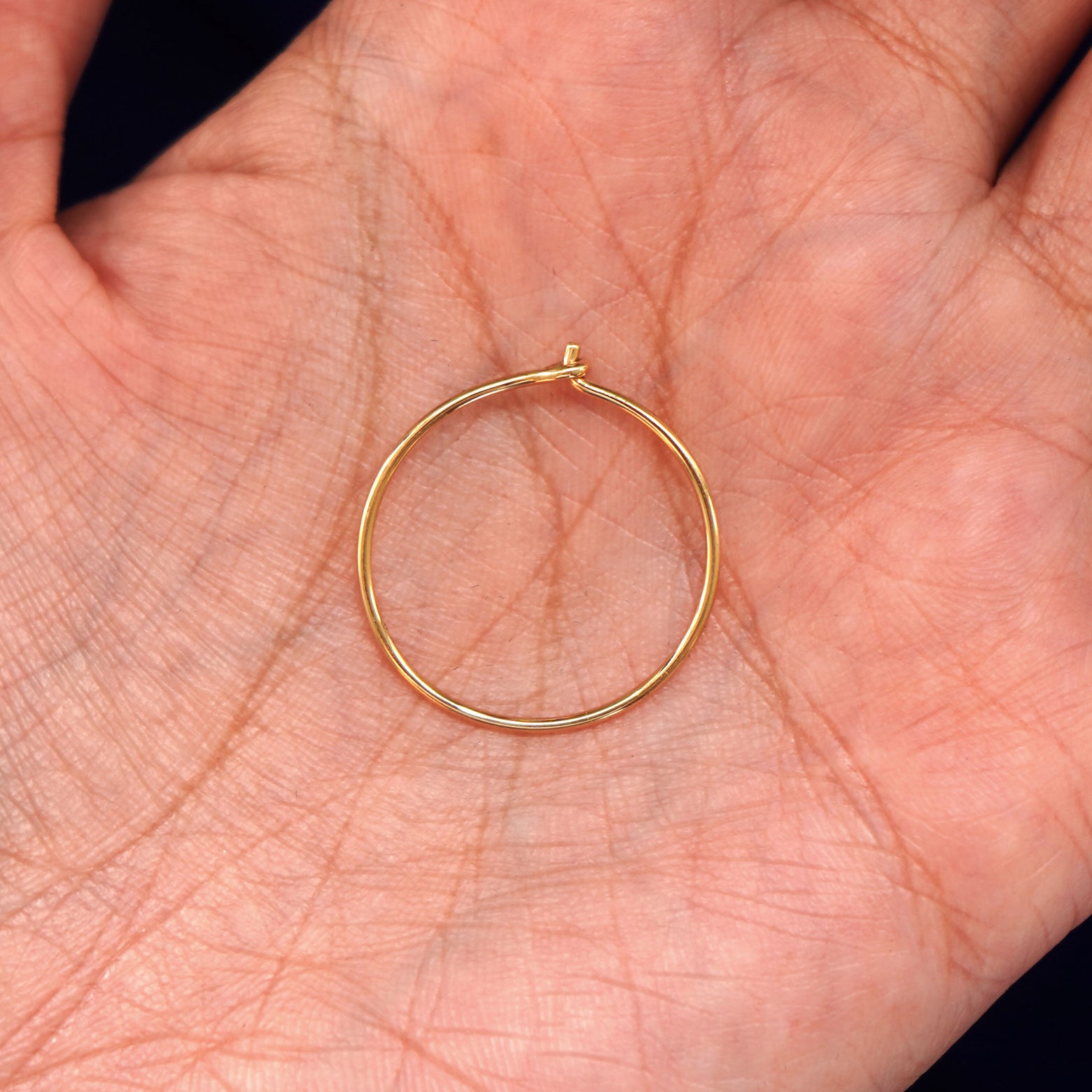 A solid 14k yellow gold Medium Hoop Earring closed in a model's palm