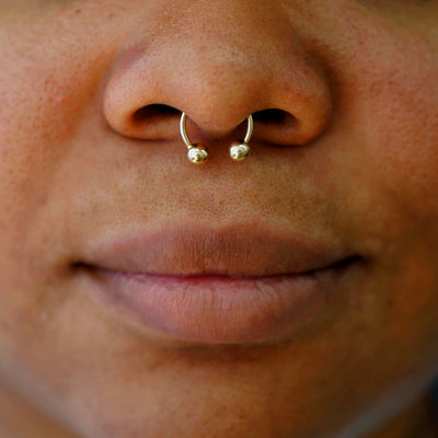 A model wearing a 14k solid gold Medium Horseshoe piercing in their septum