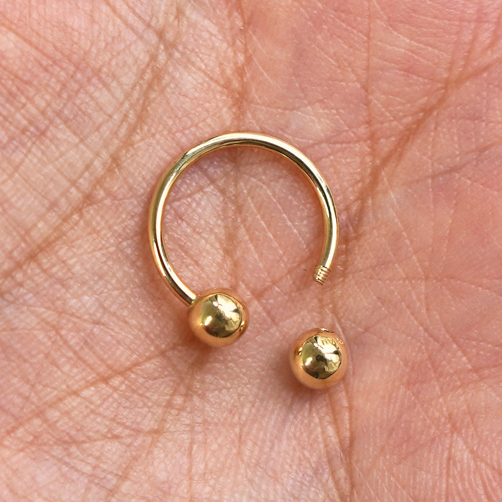 A solid yellow gold Medium Horseshoe Piercing with the externally threaded ball closure unscrewed sitting in a model's palm