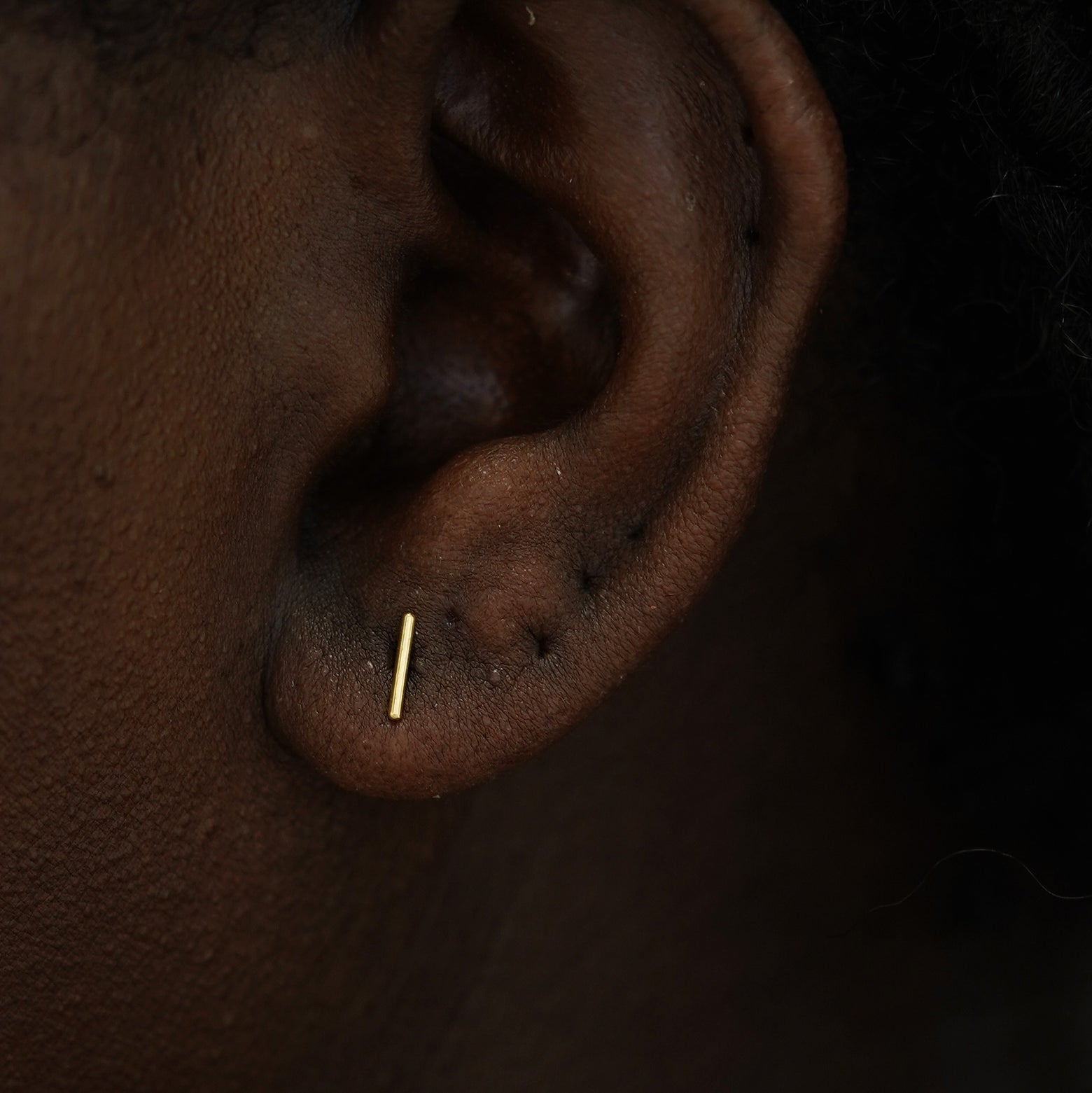 A model's ear wearing a 14k yellow gold Medium Line Earring