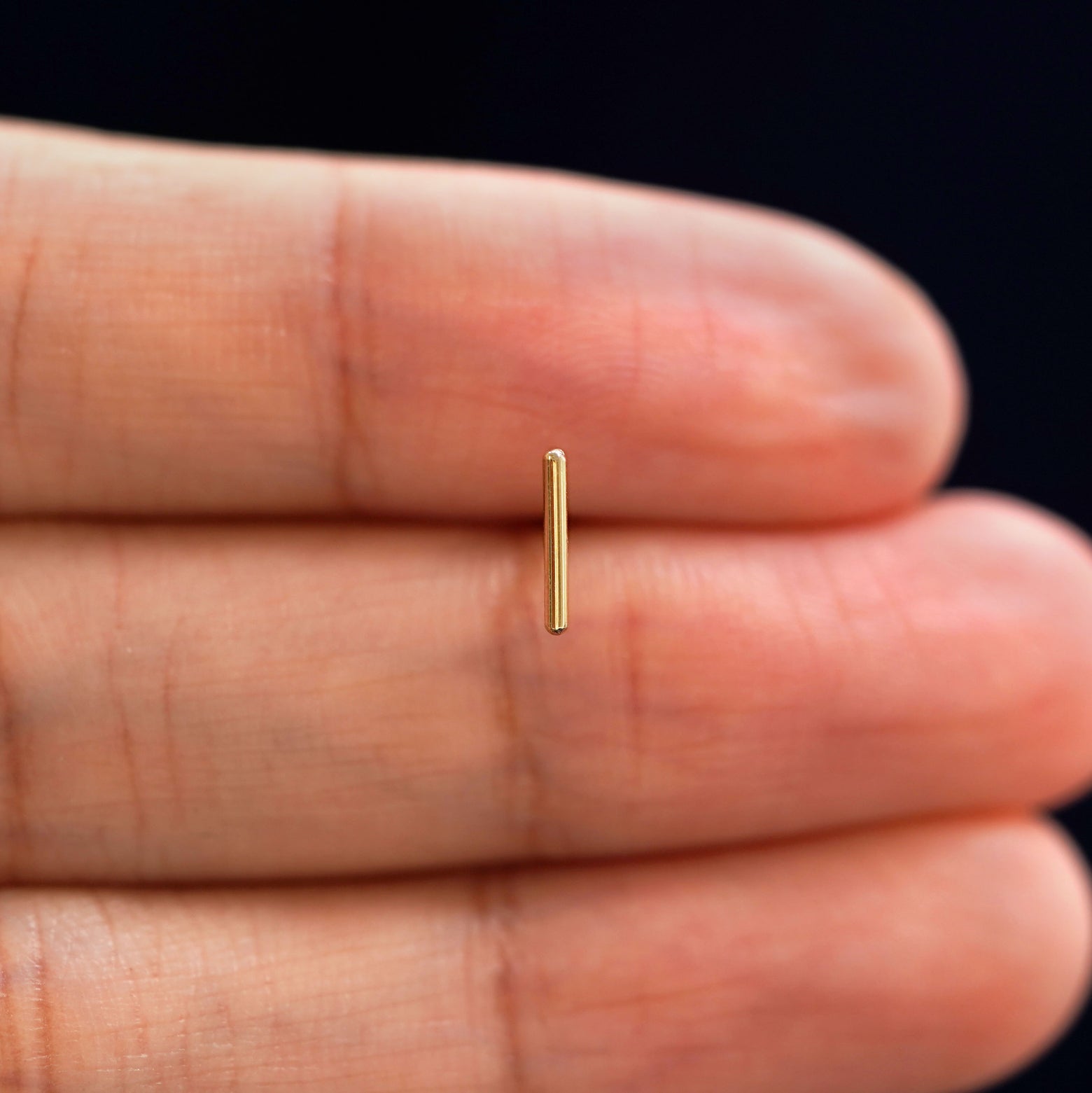 A solid 14k yellow gold Medium Line Earring in between a model's fingers