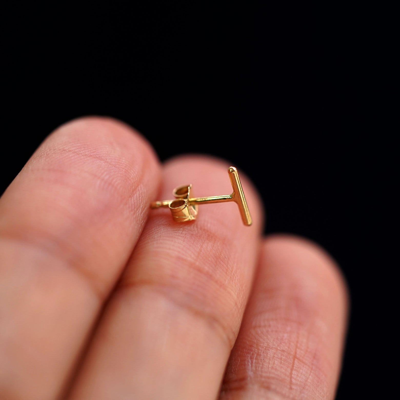 A 14k gold Medium Line Earring sitting sideways on a model's fingertips to show detail