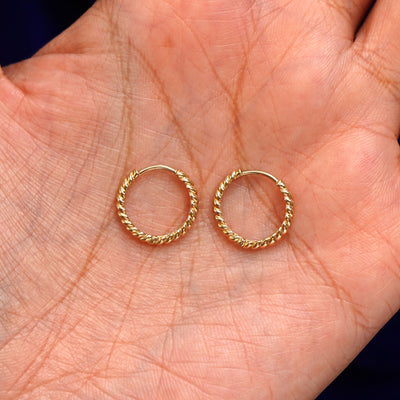 A pair of 14k gold Medium Rope Huggie Hoop Earring sitting in a model's palm