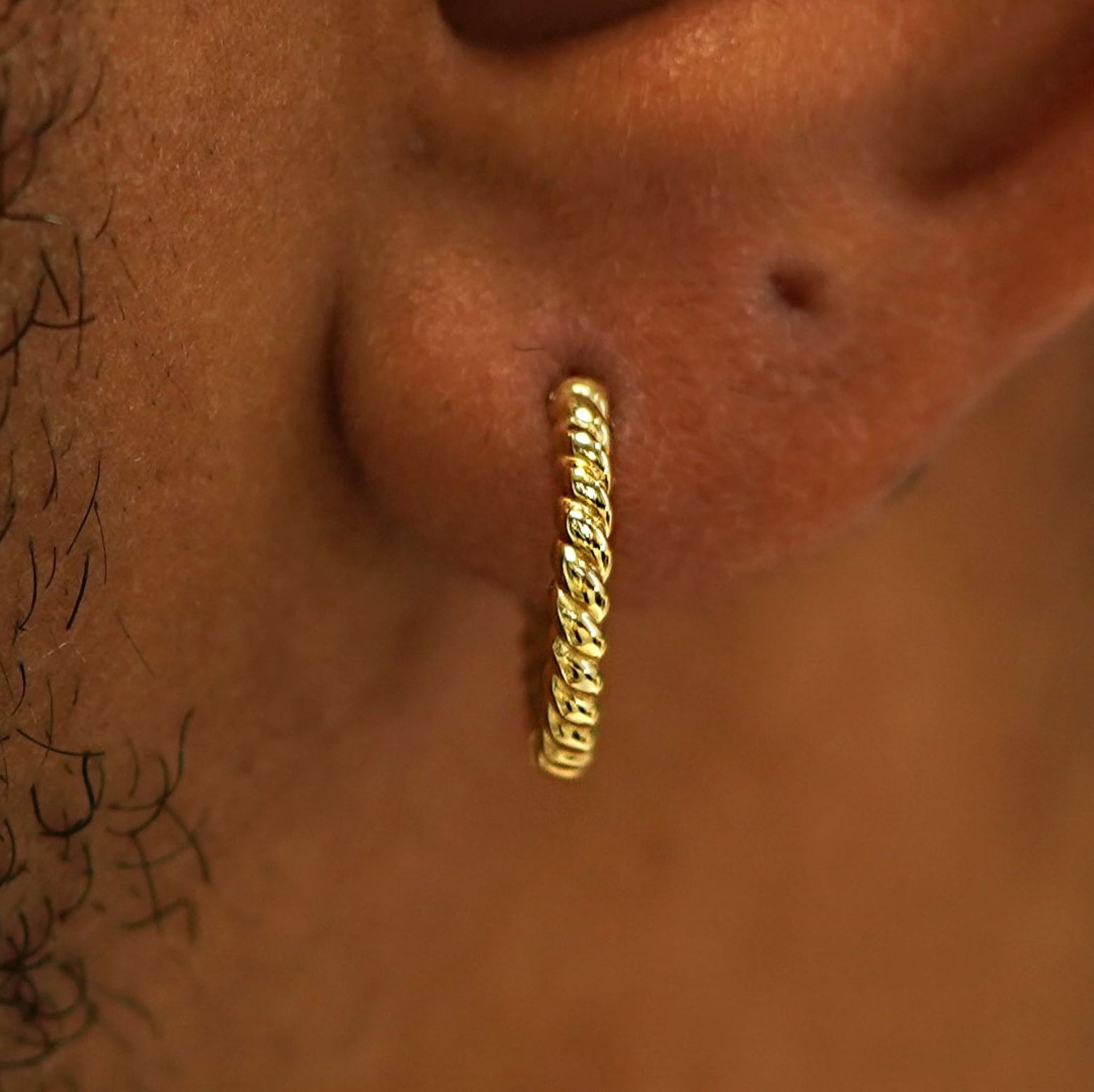 Close up view of a model's ear wearing a 14k gold Medium Rope Huggie Hoop Earring