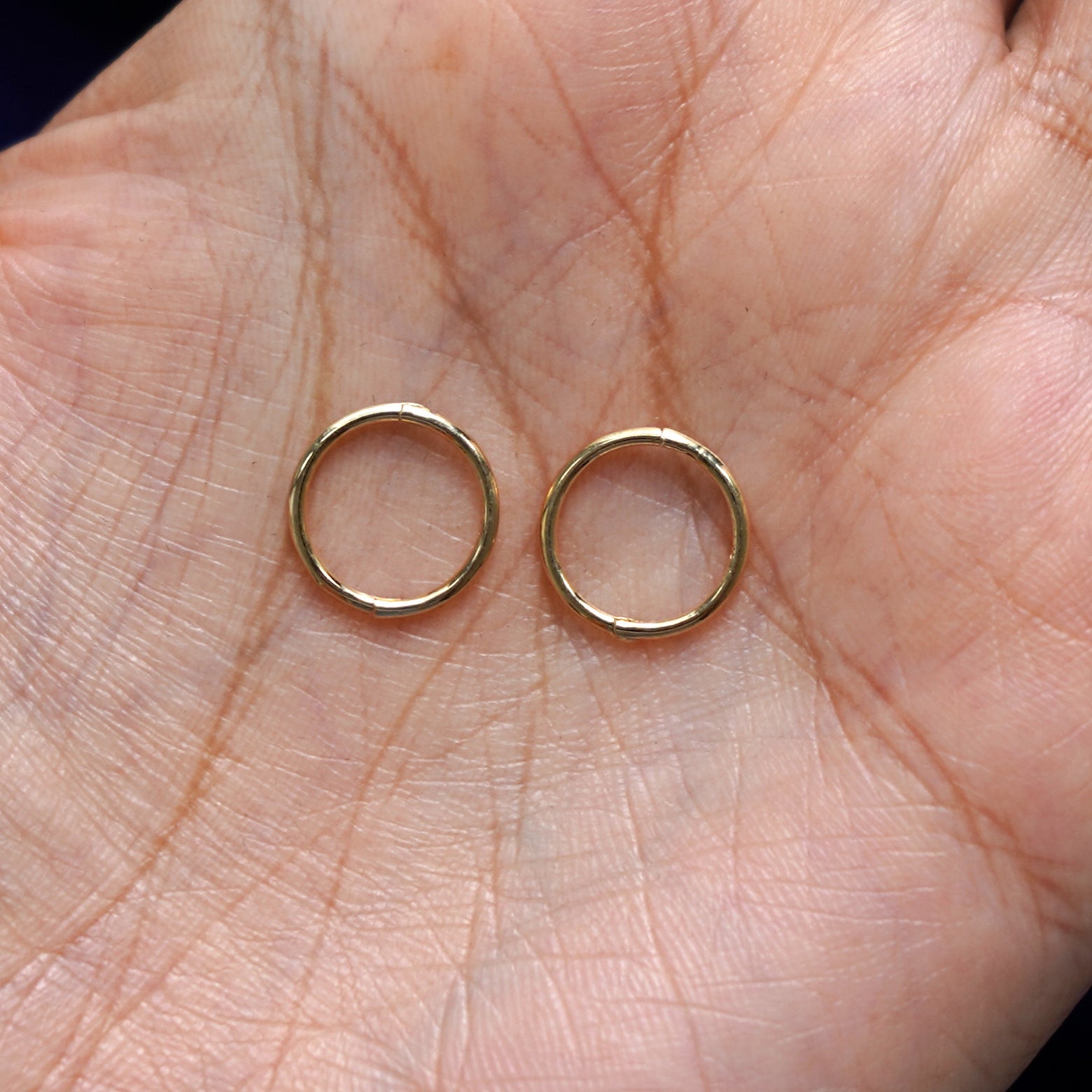 A pair of 14 karat solid gold Medium Seamless Huggie Hoops / Piercings in a model's palm