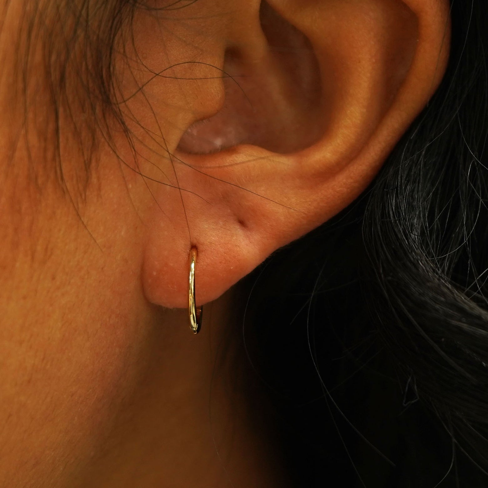 A model's ear wearing a 14k gold Medium Seamless Huggie Hoop / Piercing