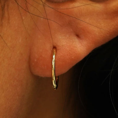 Close up view of a model's ear wearing a yellow gold Medium Seamless Huggie Hoop / Piercing