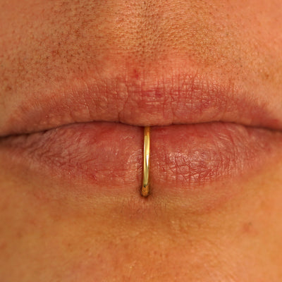 Close up view of a model's lips wearing a 14k yellow gold Medium Seamless Huggie in a center bottom lip piercing