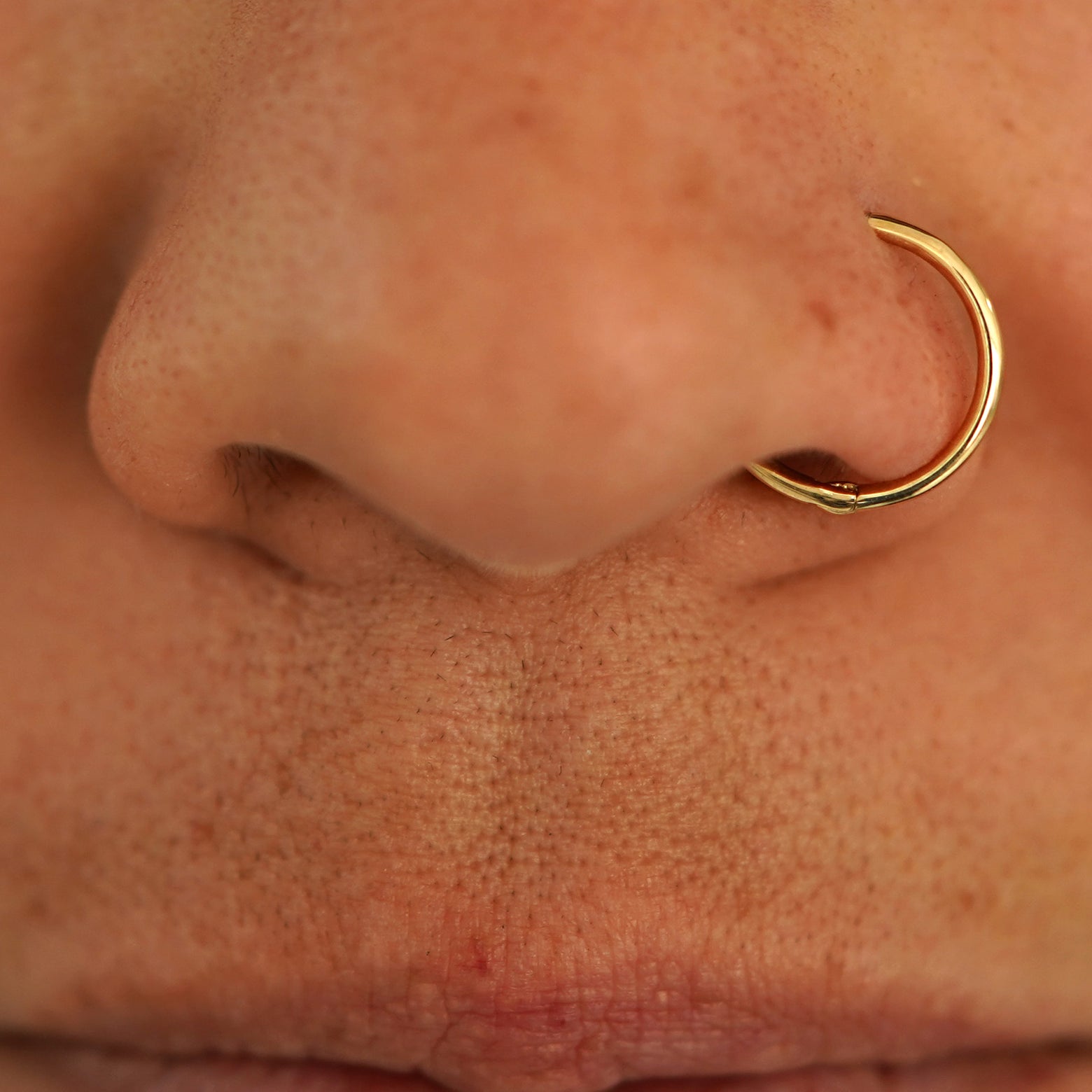 Close up view of a model's nose wearing a 14k yellow gold Medium Seamless Huggie as a nose ring hoop