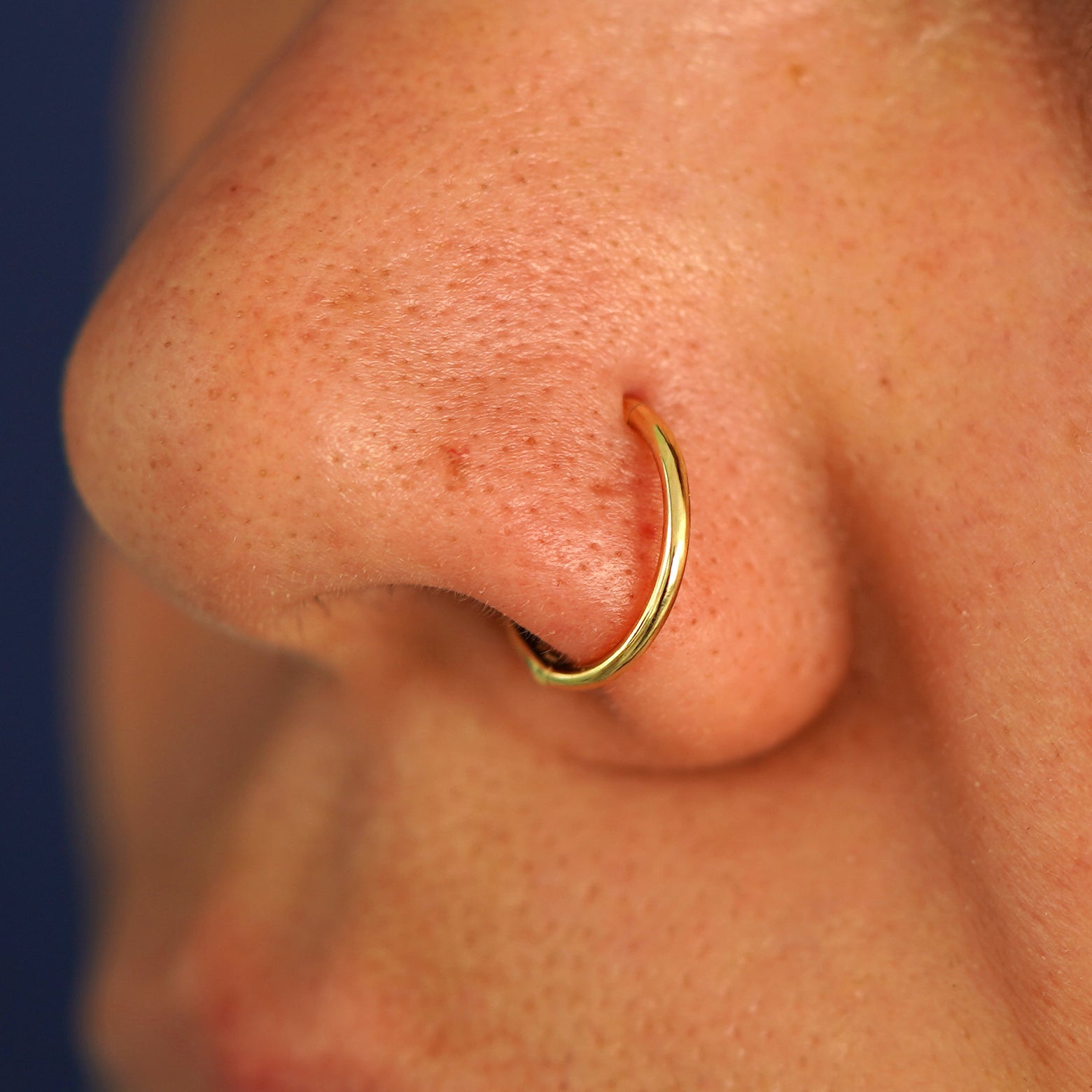 Side view of a model's nose wearing a 14k yellow gold Medium Seamless Huggie as a nose ring hoop