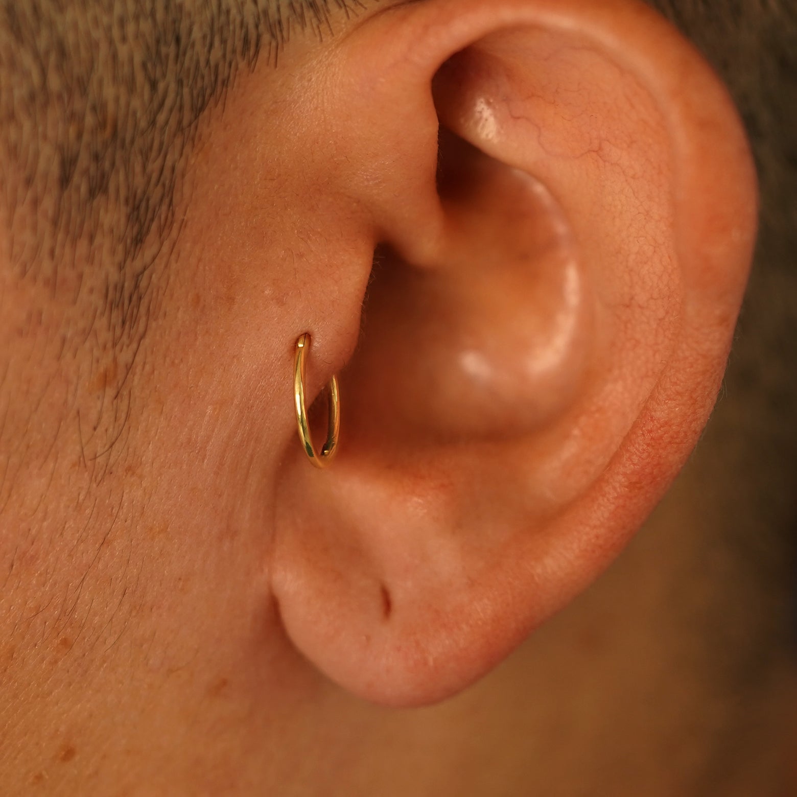 A model's ear wearing a 14k yellow gold Medium Seamless Huggie Hoop in a tragus piercing