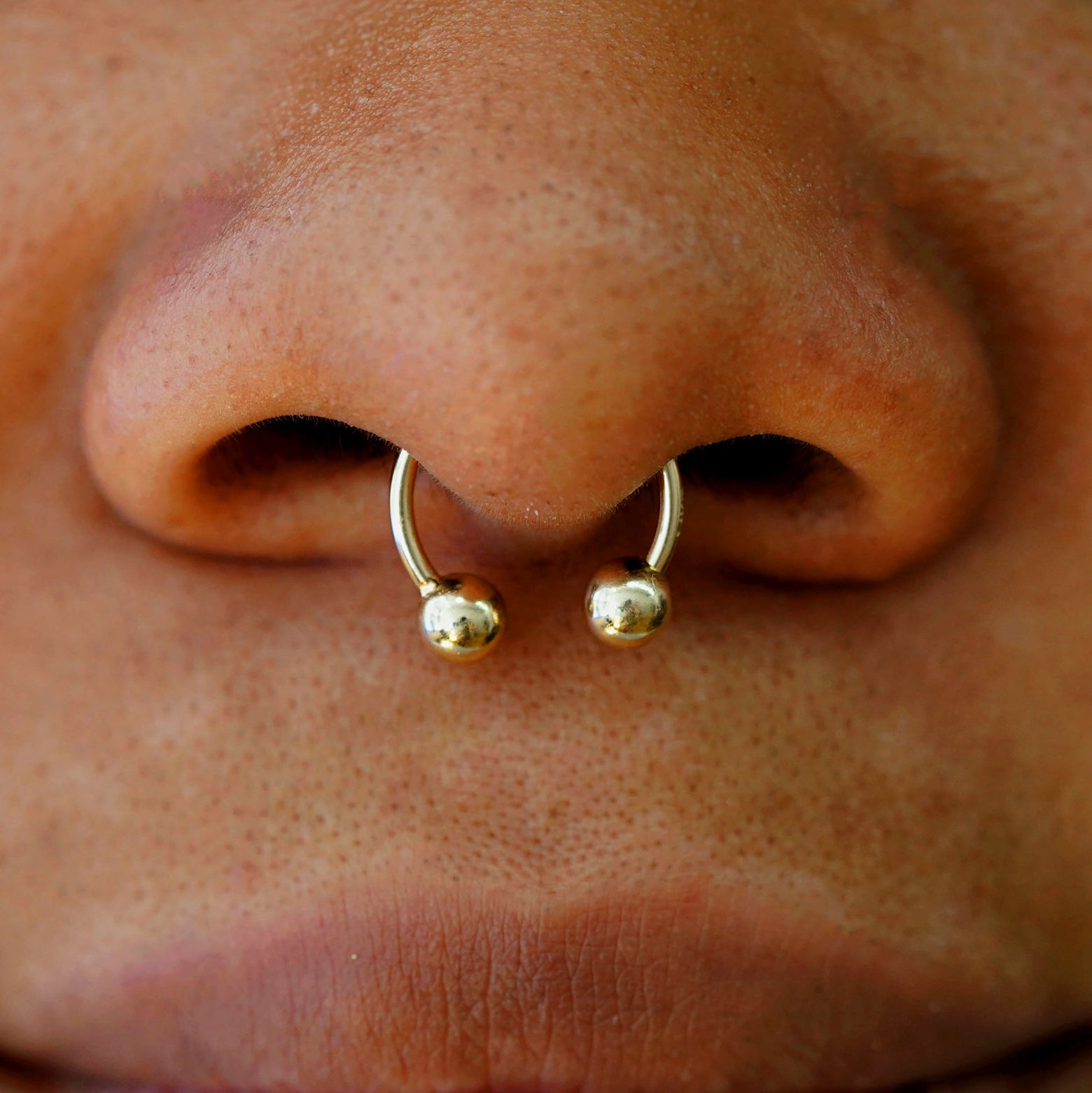 Close up view of a model wearing a yellow gold Medium Horseshoe piercing in their septum