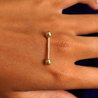 A yellow gold Medium Straight Barbell Piercing resting on the back of a model's hand