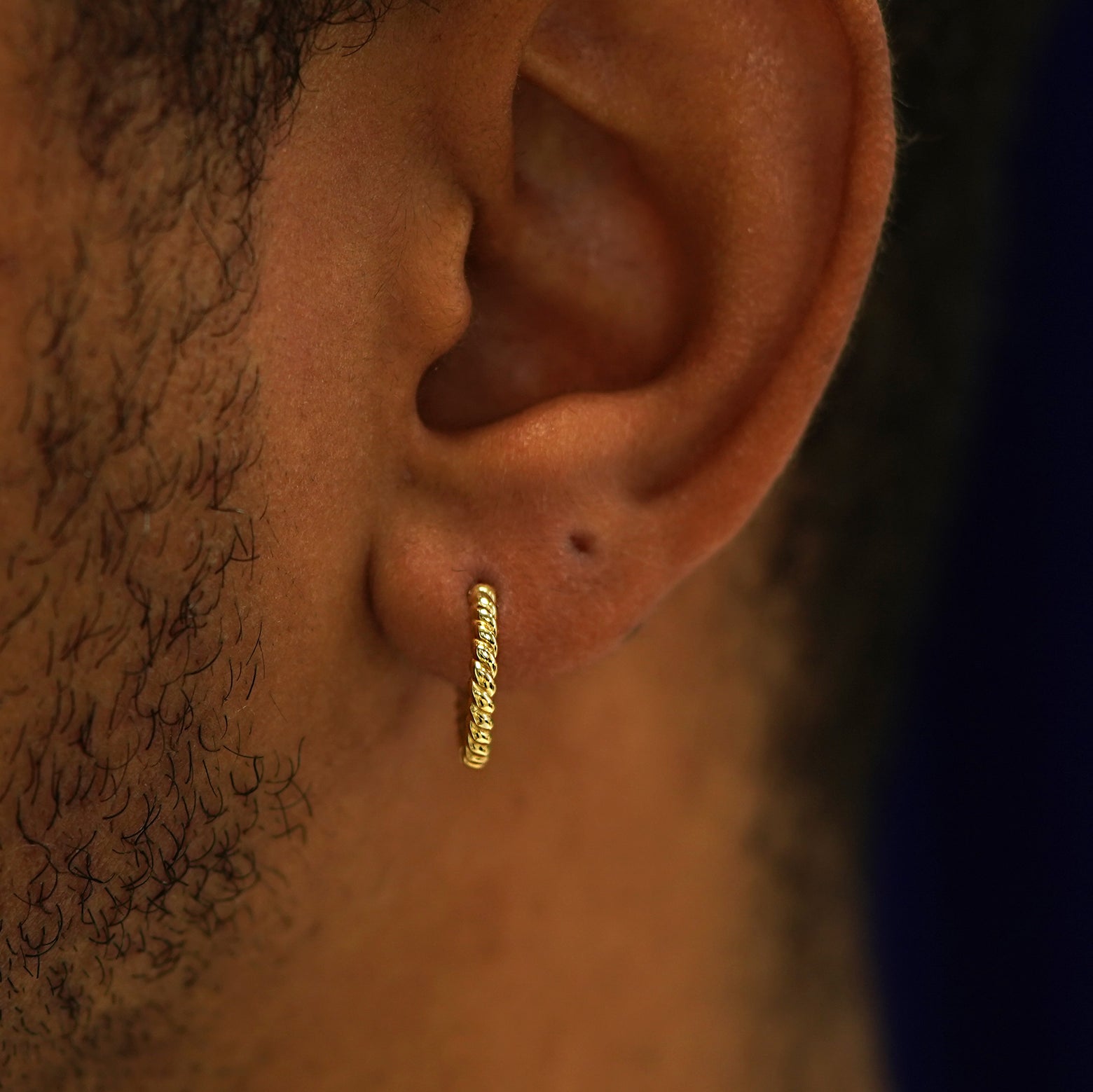 A model's ear wearing a 14k yellow gold Medium Rope Huggie Hoop Earring