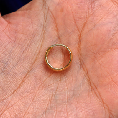 A solid 14k yellow gold Medium Thick Huggie Hoop Earring closed in a model's palm