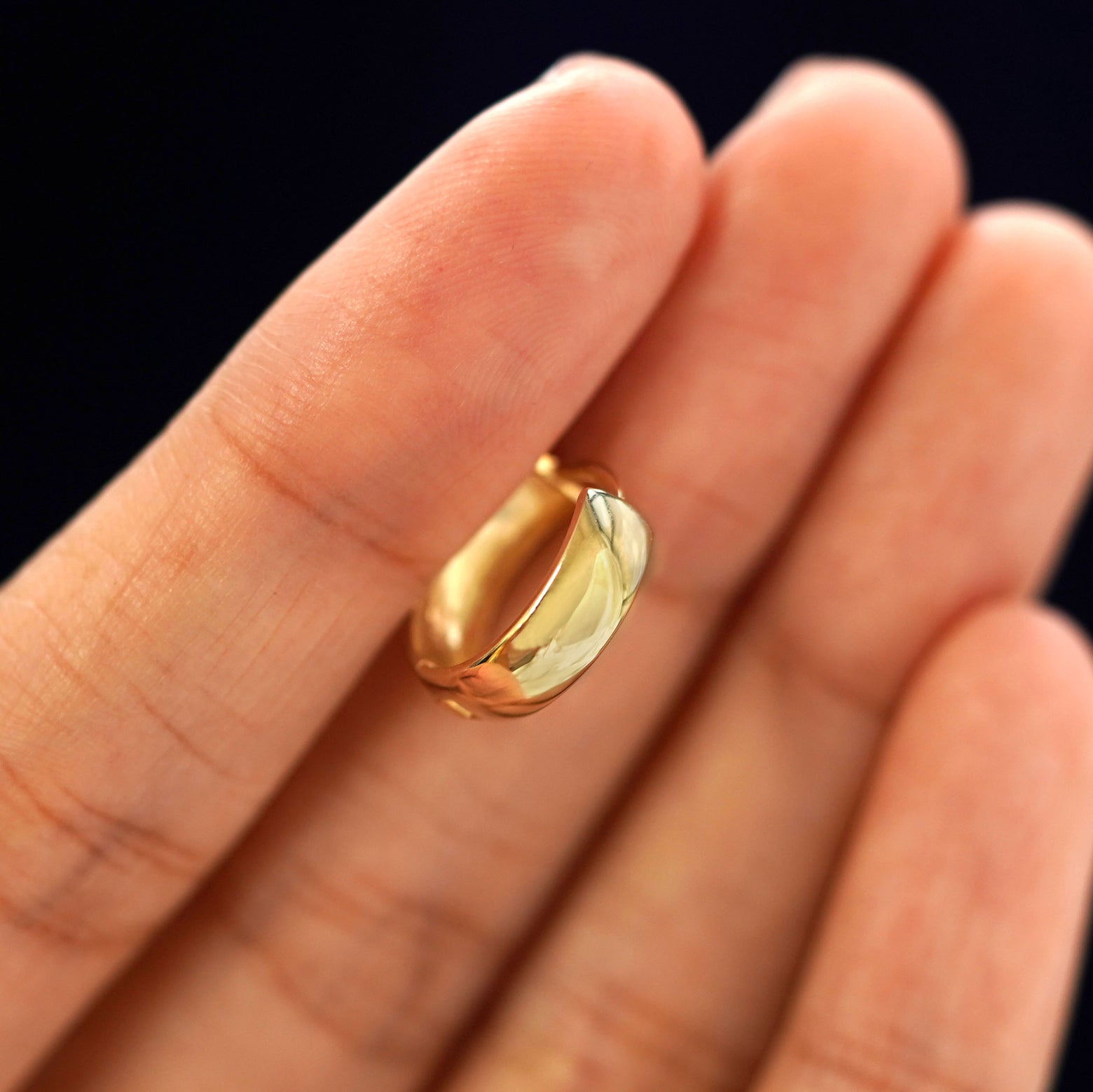 A 14k gold Medium Thick Huggie Hoop Earring held in between a model's fingers to show the hoops thickness