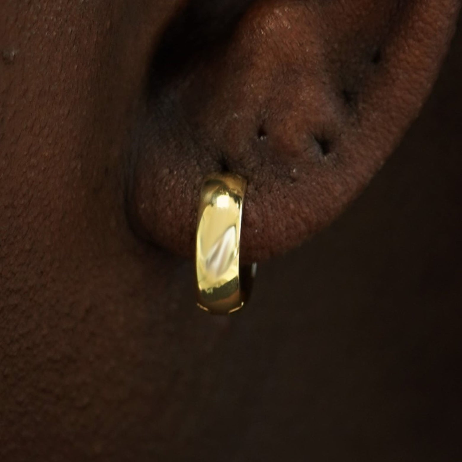 Close up view of a model's ear wearing a 14k gold Medium Wide Huggie Hoop Earring