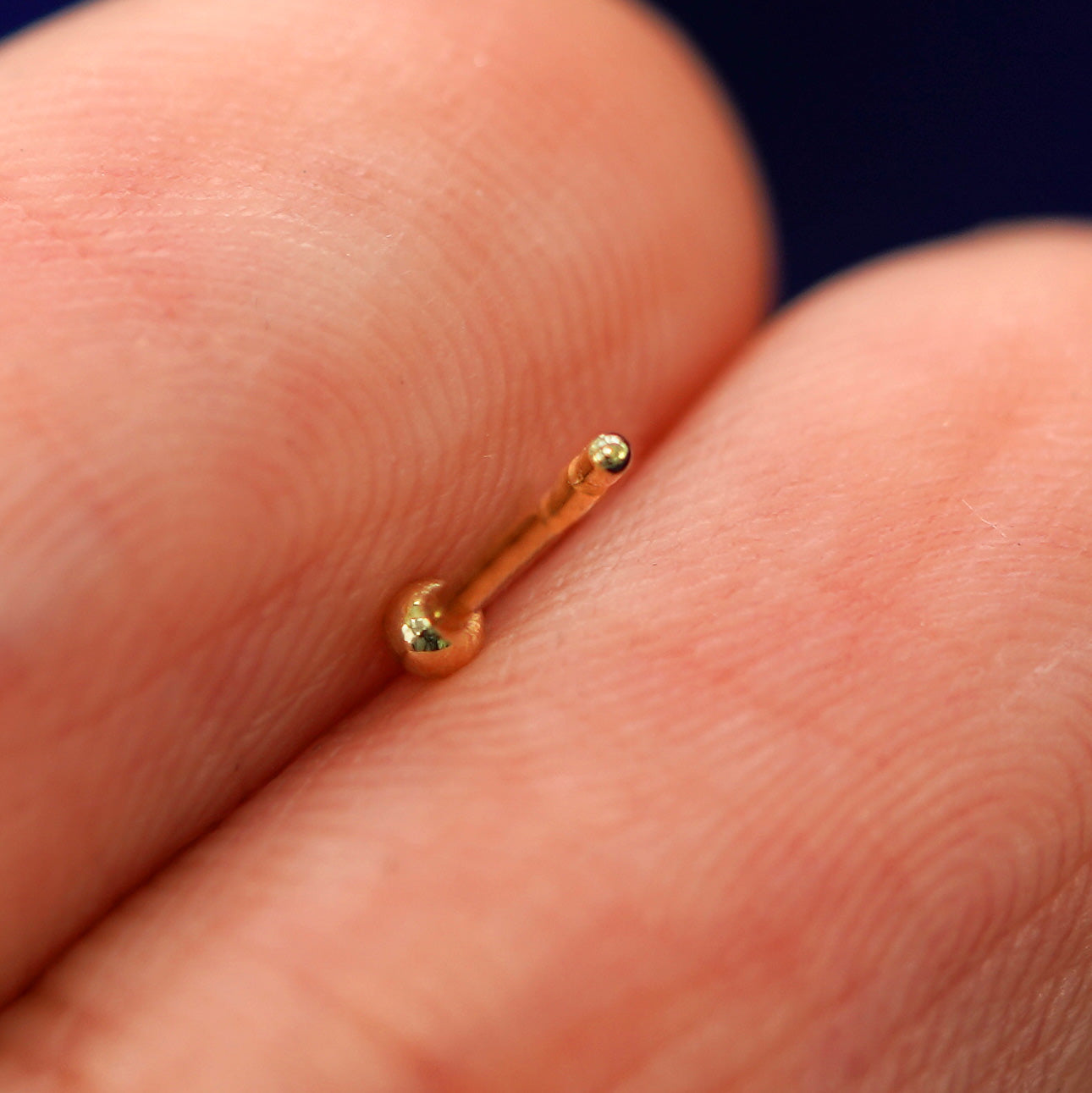 A yellow gold Mini Ball Earring laying facedown on a model's fingers to show the underside view