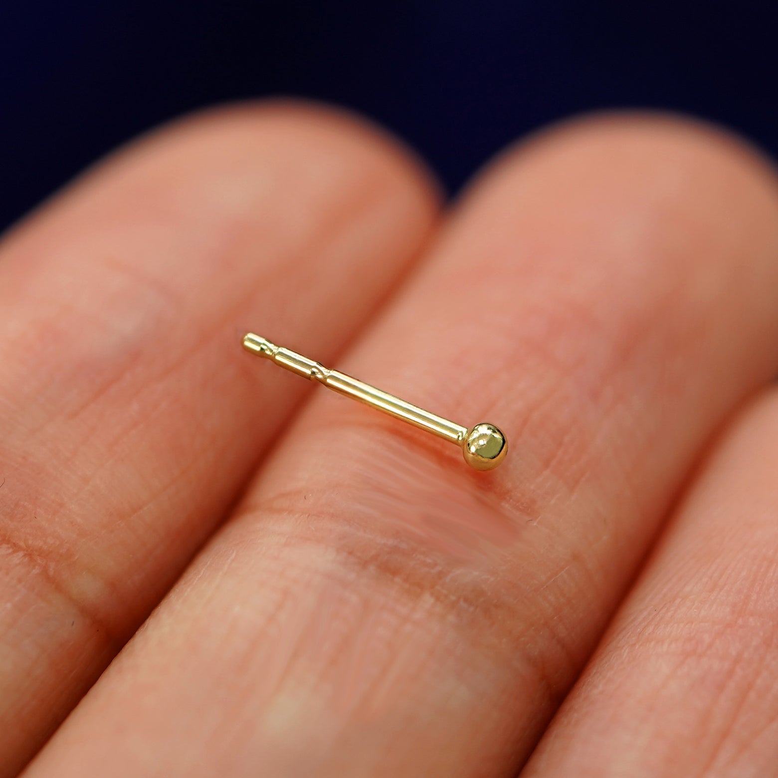 A 14k gold Mini Ball Earring sitting sideways on a model's fingertips to show detail