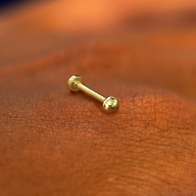 A yellow gold Mini Ball Flatback Piercing laying on the back of a model's hand