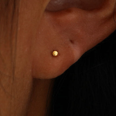 Close up view of a model's ear wearing a yellow gold Mini Ball Earring