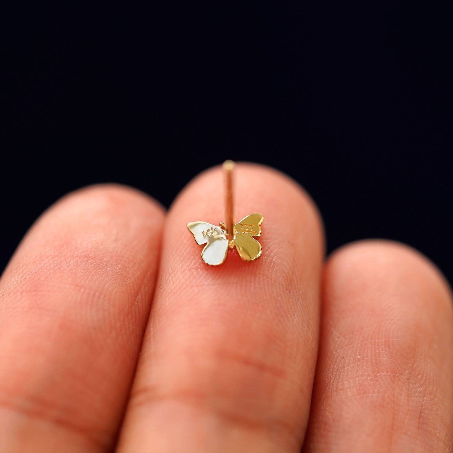 A Mini Butterfly Earring laying face down on a model's finger tip to show the post without a backing